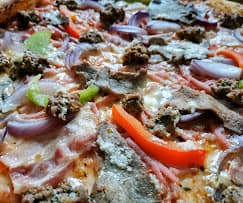 Close-up of a pizza topped with red onions, peppers, ground meat, ham, and steak.