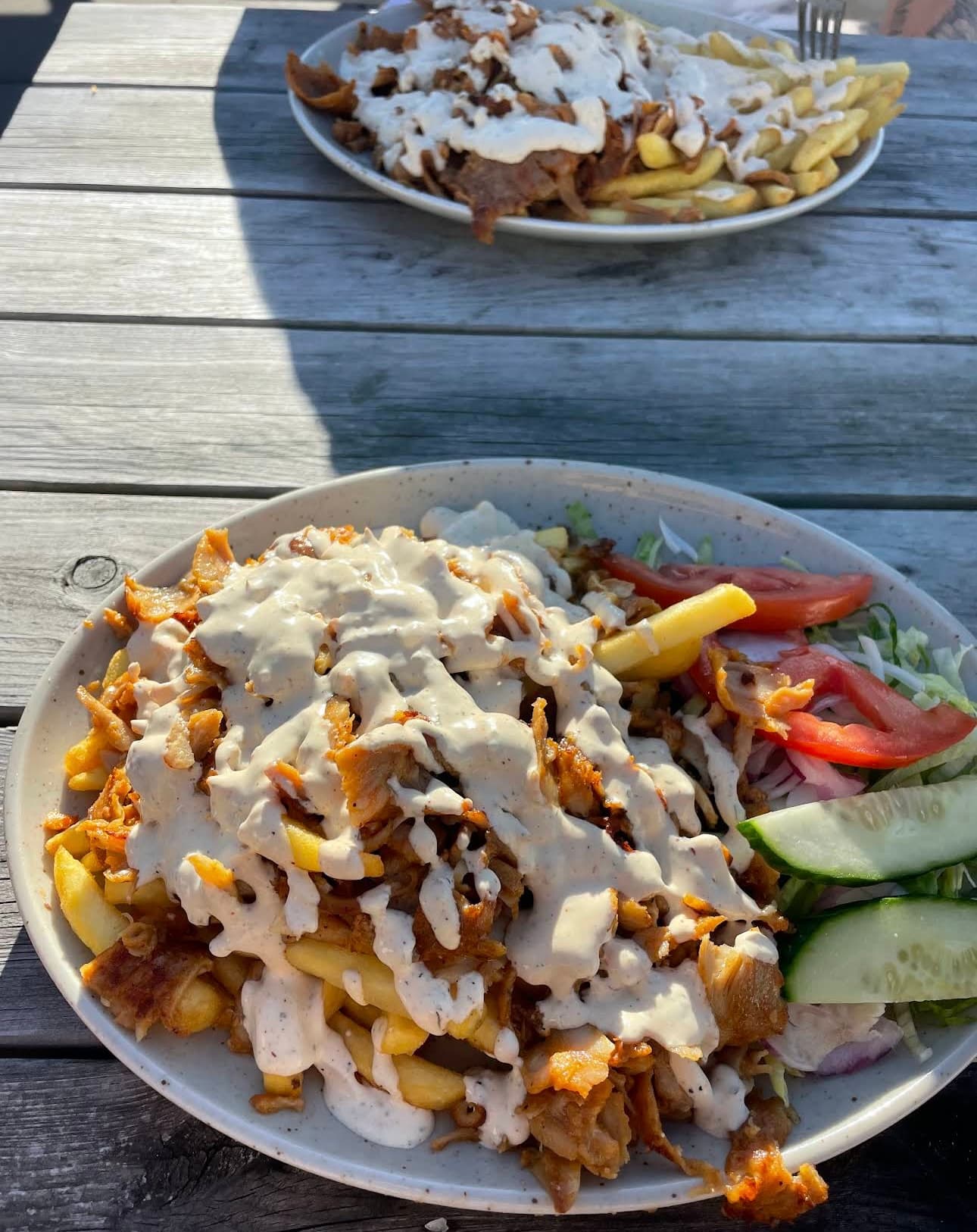 Kebab meat and fries topped with white sauce, served with salad on a wooden table.